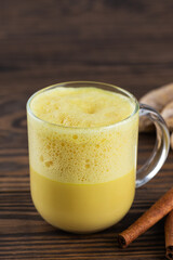 Whipped turmeric latte drink from almond milk, ginger, turmeric and cinnamon in a mug, sugar and lactose free on a wooden table.