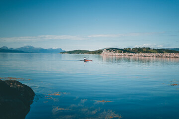 Person on a kayak with a beautiful landscape that has a bridge the background and a fjord, on a bright day with blue sky