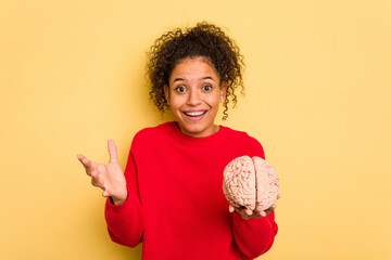 Young brazilian woman holding a brain model isolated receiving a pleasant surprise, excited and...