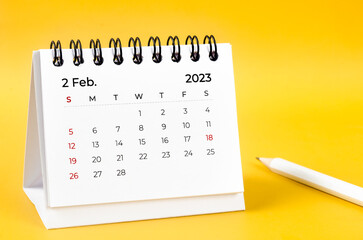 The February 2023 desk calendar and wooden pencil on yellow color background.