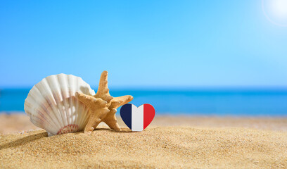 Fototapeta na wymiar Beautiful beach in France. Flag of France in the shape of a heart and shells on a sandy beach.