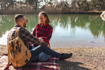 Loving couple on the lake. A young man and woman are sitting on a blanket by the lake. Young family on a picnic in nature near the water.
Valentine's Day. Concept of love and family.