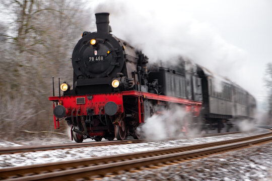 Fast steam train in motion on the Ruhr valley line (Ruhrtalbahn) between Schwerte and Winterberg. Blurred Engine with full speed and puff of smoke in a curve near Arnsberg on a cold snowy winters day.