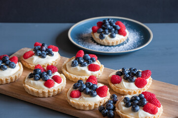Seven small custard tarts on a cutting board in front of an icing sprinkled blue plate.