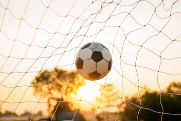 Naklejka premium A ball in goal net for street soccer football under the sunset ray light. Film picture style.