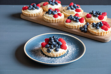 Seven small tarts on a cutting board behind an icing sprinkled blue plate in the center.