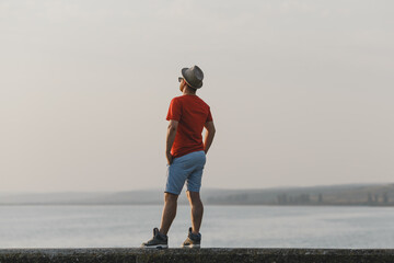 Young hipster man enjoying the picturesque view of Italian lake  in hat, red t-shirt, blue shorts 