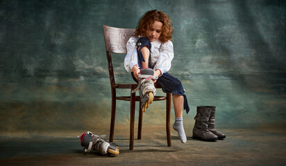 Full body portrait of positive little girl, kid learning to ride on roller skates isolated on dark background. Retro vintage fashion style concept