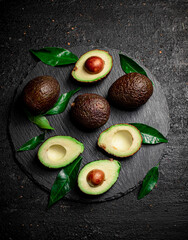 Pieces of fresh avocado with leaves on a stone board. 