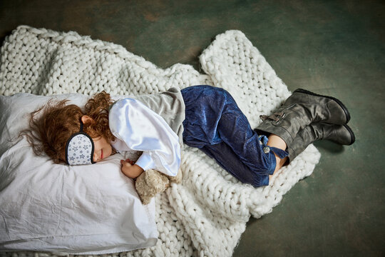 Ariel view of cute little girl in clothes sleeping on white blanket. Concept of napping day, dreams, happy childhood.