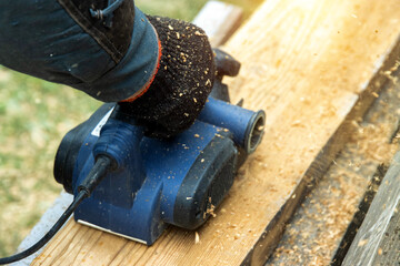 A man works with an electric tool with an electric planer, cleans old wood. Industry, close-up