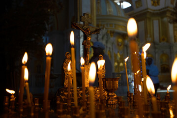 Cross with crucifix in focus, lit wax candles, funeral service, prayers for salvation of soul. Memorial service, an Orthodox church. Concept of Christian religion. - obrazy, fototapety, plakaty