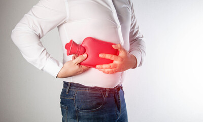 The man holds a heating pad with hot water on the abdominal wall on the right. Relieve muscle...