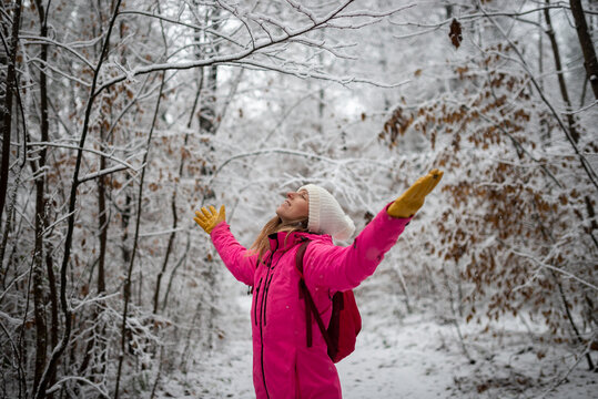 Young woman in pink winter jacket celebrating and enjoying life standing in wite snowy nature