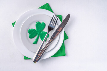St. Patrick's Day festive table setting. Plate and cutlery with green napkin, shamrock symbol, gold horseshoe decor for luck. Patrick Day menu background, party invitation, top view copy space