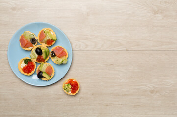 Tartlets with salmon and caviar on wooden background, top view