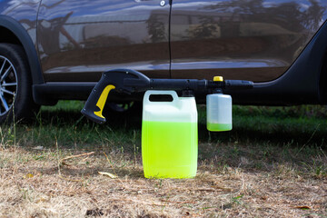 a canister with shampoo and a nozzle for a high-pressure washer a foam generator against the background of a car. Car wash and care. Copy space for text