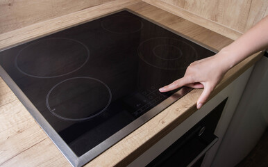 A woman's finger presses the inclusion of a modern induction hob in the kitchen. Electric induction...