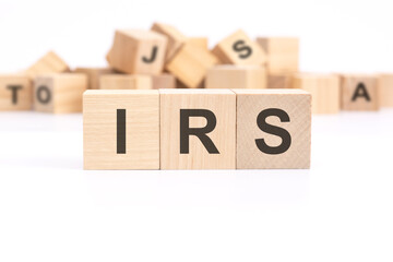 text IRS - internal revenue service - is written on three wooden cubes standing on a white table. in the background - a mountain of wooden cubes with letters.