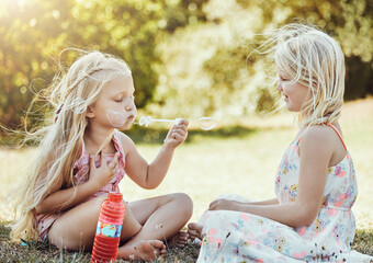 Nature, girls and friends blowing bubbles in a green garden being playful, happy and fun together. Happiness, holiday and sisters playing on the grass in an outdoor park in summer in Australia.