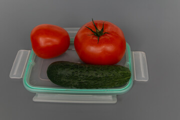 Ripe and beautiful tomatoes and cucumbers in a plastic food container. Close-up. Vegetarian food.