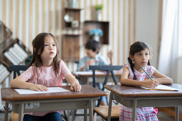 Cute little girl using color pencil drawing on paper in art study class at elementary school. Group diverse student to listen teacher in classroom . Children education and learning concept.