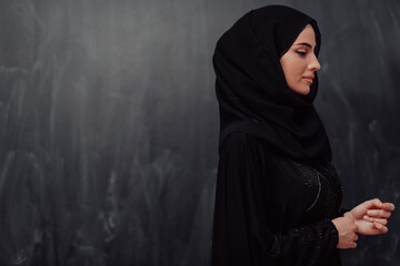 Portrait of beautiful muslim woman in fashionable dress with hijab in front of black chalkboard...