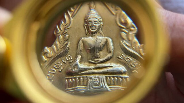 Pocket magnifier lens looking at Thai amulet buddhist sacred talisman for fortune and protection buddha figure meditation gesture close up. Traditional Thai religious superstition concept