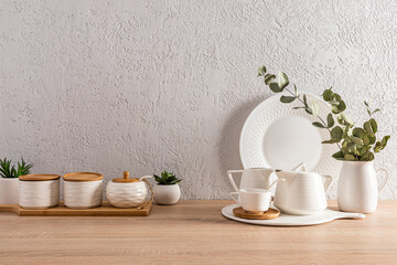 white ceramic dishes and jars with wooden lids on the countertop. kitchen background. grey textured wall. a place for a text.