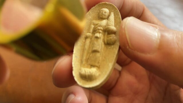 Pocket magnifier lens looking at Thai amulet buddhist sacred talisman for fortune and protection monk figure standing gesture close up. Traditional Thai religious superstition concept