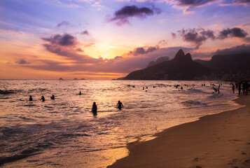 Silhouettes of beachgoers in Rio de Janeiro, Brazil playing on the sand and in the water of the...
