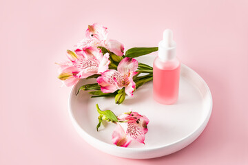 a matte white bottle with a floral natural cosmetic for face and body skin care stands on a white ceramic plate with pink flowers.