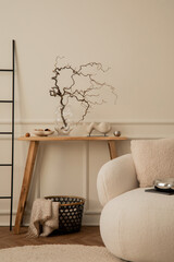 Creative composition of living room interior with wooden bench, white sofa, glass vase with branch, black basket, beige plaid, chrom sculpture, round rug and personal accessories. Home decor. Template