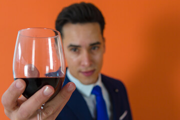 extreme close up image of a wine glass being holding by an elegant man dressed in suit ahead an orange background