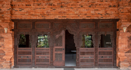 Fototapeta na wymiar Gebyok is surrounded by brick walls. Gebyok is one of the typical Javanese furniture, which is generally made of teak wood. Used for the door of the house. One of the two doors is opened.
