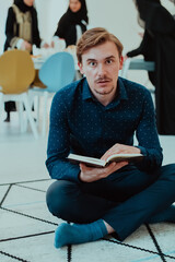 young muslim man sitting on the floor while reading holy book Quran before iftar dinner during a ramadan feast at home