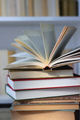Stack of books on the table, reading glasses and e-reader on the table. Bookshelf in the background. Selective focus.