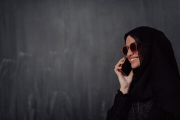 Young modern muslim business woman using smartphone wearing hijab clothes in front of black chalkboard