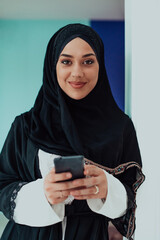 Young modern muslim business woman using smartphone wearing traditional hijab clothes at home