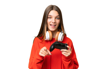 Teenager caucasian girl playing with a video game controller over isolated background surprised and pointing front