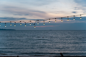 light bulbs on string wire decoration at the party event festival on the beach at sunset. Outdoor holiday background. Copy space.