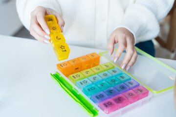 Woman's hands holding daily and weekly pills organizer on the table. Taking daily medicine...