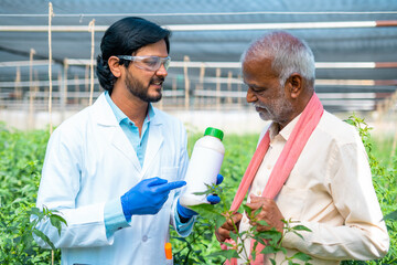agro scientist at greenhouse explaining by hoilding fertilizer or pest control bottle to village...