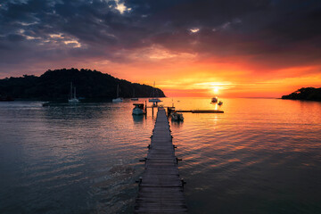 Obraz premium Beautiful sunset over tropical sea and wooden pier, sightseeing boat and tourist enjoying in Koh Kood Island