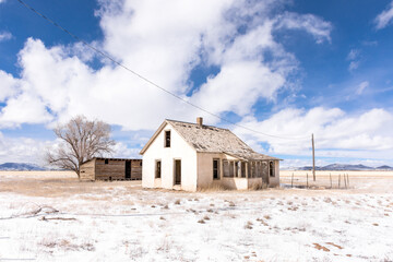 Abandoned homestead with tree and out building on potato farm, San Luis Valley, Colorado, with blue sky, clouds, and snow on a winter day