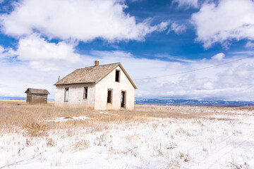 Abandoned homestead with out building on potato farm, San Luis Valley, Colorado, with blue sky, clouds, and snow on a winter day
