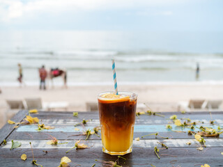 A glass of fresh iced orange americano decorated with sliced ​​orange served on wooden table on the beach background, seascape view. Cold black coffee with orange juice, mixing mocktail drink menu.