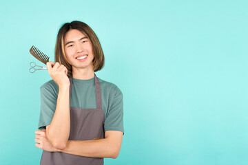 Asian hairdresser with scissors and a comb smiling at camera