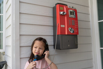 Children stand at coil red telephone box holding a telephone handset and wait for a phone call