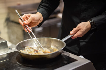 man chef cooking fried shrimp in frying pan on kitchen